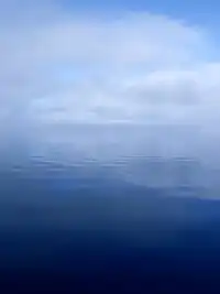 A calm, flat river surface with clouds and fog obscuring the horizon line