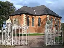 Small brick Neoclassical chapel behind ornate iron gates