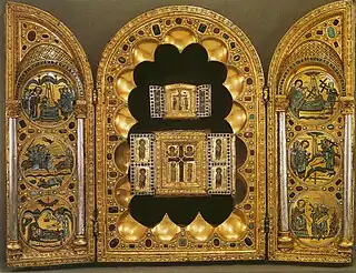 A golden, bejewelled triptych. The left and right wings each show three inlaid circular images; the centre panel has a scalloped surround housing two older triptychs, each containing a wooden Cross and showing Byzantine-style Greek lettering.