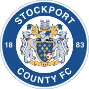 The words "Stockport County FC" in a circle (along with "18 on the left and "83" on the right) surround the main crest consisting of a shield featuring a hat and castle on top along with two lions rampant either side.