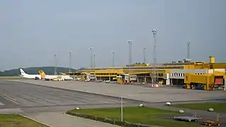 A mostly yellow airport terminal seen from the apron; furthest away there are two jet planes parked