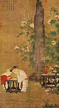 A portrait oriented painting depicting two young children, a boy and a slightly older girl, playing with figurines on a table in a garden. Behind them is a tall rock flanked by branches of a flowering tree.