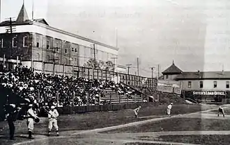 A black and white photograph of home plate and the left field bleachers at a ballpark