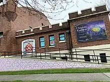 at a street corner, tacoma armory is a large brick building. a ramp leads to a door that is painted red and white with the tacoma arts live logo