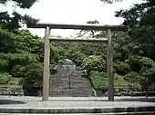 Stairs leading through a wooded area to a stone structure beyond a large torii.