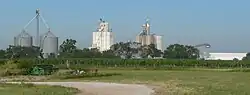 Metal and concrete grain bins and elevators; cornfield in foreground