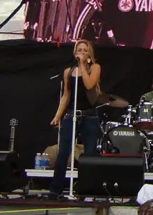 A woman sings into a microphone, her entire height shown.