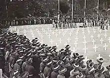 Soldiers in slouch hats stand around a square of white crosses during a ceremony at a war cemetery