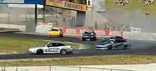 five sports cars slide sideways around a corner