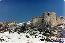 Ruins of the tower and the walls of a fortress made of stone on a hill covered with snow