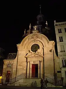 The church illuminated at night with the spire and the toit à l'impèriale rising behind the cross-topped arch