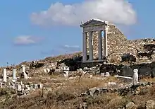 A hillside littered with broken columns. An intact set of columns, supporting a pediment, still stand.