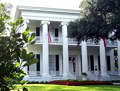 A white Greek-revival-style mansion with 6 tall columns visible at the front and two stories