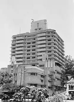 Rounded building with two visibile facades; the lower floors have a concrete exterior with grooved, triangular niches and round, protruding edges. The uppermost floors, slightly less prominent, have a glass exterior.