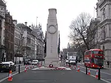 A stone monument in the centre of a street with traffic passing