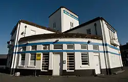 A white brick building with two horizontal blue stripes, and a rounded quarter-circle frontage