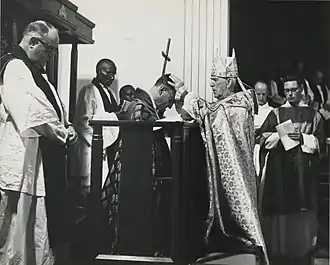 kneeling man being blessed by standing man, the latter in cope and mitre