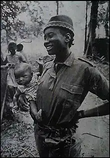 Photograph of Titina Silá, holding a baby, while dressed in her militia uniform