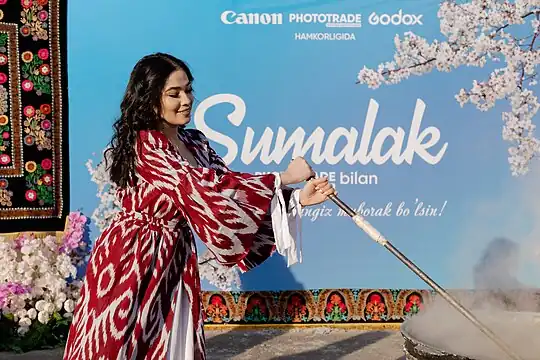 A woman in traditional clothes stirring sumalak during  Navruz celebrations