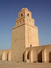 A square stone tower rises high above a wall.