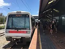 Electric multiple unit train at a brick station platform with a crowd of people and shelter overhead