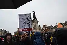 crowd in the rain, poster of Trump face, Baby Trump balloon, around statue of Marianne