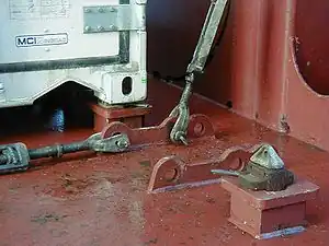 Twistlocks on deck of container ship.  Foreground: unlocked; background: locked.  The turnbuckles are "lashing rods" used for shoring