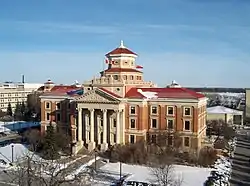 Exterior of building clad in red bricks with white trim, four marble pillars at the front entrance and a two-tiered dome on the roof