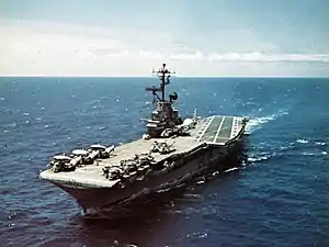 Medium-size aircraft carrier with numerous aircraft on its flight deck.