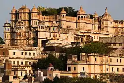 Side view of an ornately decorated palace with several towers on a hill over a city of terraced houses.