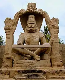 Brown stone statue of smiling deity sitting cross-legged under arch