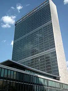 View of the building from the southwest, with the Dag Hammarskjöld Library in the foreground. The western facade at left is made of glass, while the southern facade at right is clad in stone.