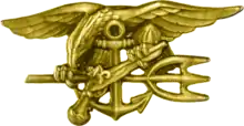 A gold image depicting an eagle perched on an anchor, clutching a trident with one claw and a gun in the other.