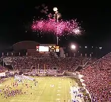 Football players enter a packed stadium with fireworks erupting at one end