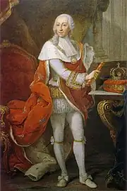 Full-length portrait of a bewigged monarch in white tights and a red robe with his crown sitting on a table