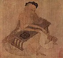 Elderly Chinese man, seated at a low writing desk and holding a scroll