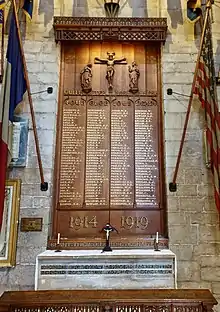 Names are written in gold on a carved oak panel above a stone altar. The flags of Great Britain, France, USA, and the British Legion, surround the panel.