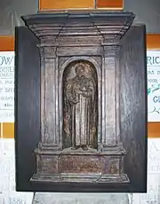 A dark terracotta relief of a man holding a long partly unrolled scroll