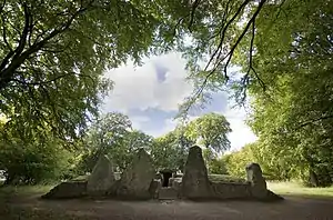 a pathway flanked by standing stones leads up to a stone entrance