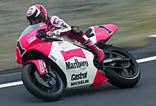 Wayne Rainey wearing motorcycle overalls and a crash helmet riding a red and white sponsored motorcycle on a race circuit in 1992