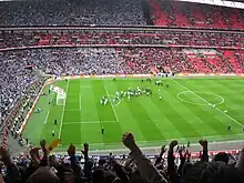 A full football stadium, with spectators in the left half wearing blue, and those in the right half wearing red