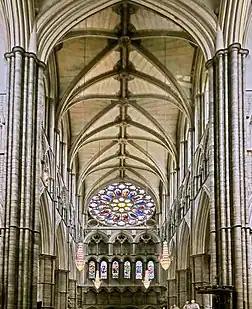 The inside of Westminster Abbey north transept, with a high vaulted ceiling and a rose window at the end.