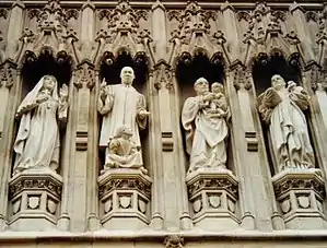 Photo shows four of ten statues above the door of the Abbey. They are carved in a realistic and lifelike manner, full of action. Elizabeth wears nun's habit and holds a cross, King preaches with a little black girl at his feet, Romero holds a naked indigenous baby, Bonhoeffer carries a book. They are set in traditional Gothic niches with ornate carved canopies.