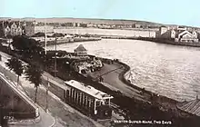 An old photograph of a tram running along a waterfront road.