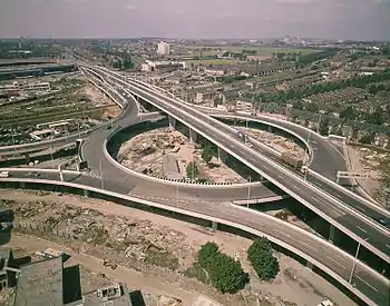 Aerial view of elevated roundabout with flyover passing above and slipways joining from three directions. Construction appears to have recently finished.