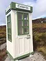 Photograph of a green-and-white telephone booth with a banner that reads "Telefón"