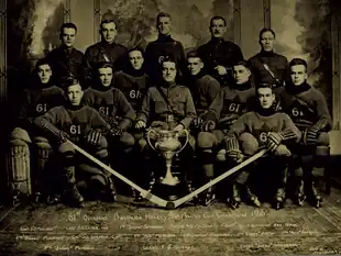 Black and white photo of a hockey team seated behind a large trophy