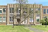 An old two-story school front with a large tree in the foreground