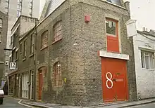 A two-story brick building on a street corner with red doors.