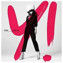 A portrait in black, white and pink, featuring English singer Yasmin posing in front of a bold, pink-coloured 'Y!'. She is wearing a matching black jacket and pants with a pink shirt underneath in addition to a winter headpiece on her head. To her right stands 'YASMIN_FINISH LINE'.